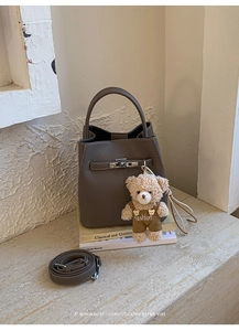 Detail of dark brown leather bucket bag with metal lock and cute bear charm accessory