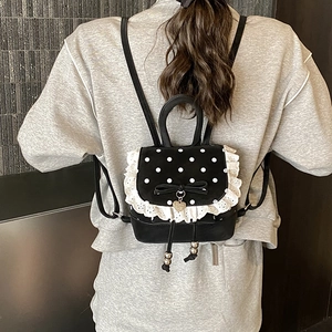 Dettaglio mini zaino a pois con bordi in pizzo bianco e ciondolo a cuore e fiocco