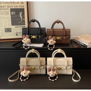 Close-up of litchi texture handbags with golden ring buckle and plush bear pendant