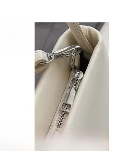 Detailed close-up of smooth silver zipper and metal buckle on cream shoulder bag