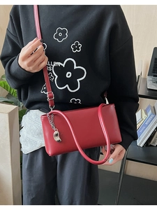 Close-up of red rectangle shoulder bag with silver chain pendant on a black outfit