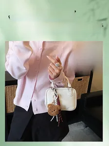 Close-up of white crossbody bag with cute plush bear pendant and textured leather finish