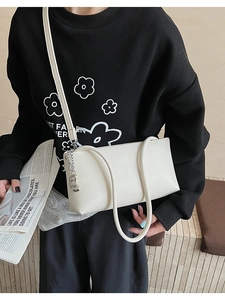 Detail of white faux leather shoulder bag with silver pendant shown on black hoodie