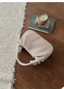 Detailed texture of a cream pleated handbag with knotted handle on a warm wooden floor
