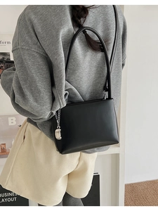 Detail of minimalist black leather crossbody bag with a metallic silver pendant charm