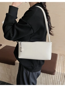 Detail view of cream shoulder bag with minimalist silver metal pendant on its side