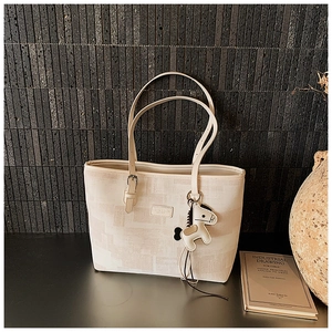 Detail of cream tote bag with contrast charm and adjustable strap on a grey background