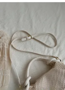 Detail of adjustable strap and golden metal buckle on pleated cream handbag
