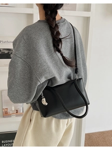 Detail of minimalist black leather tote bag with silver moon pendant on shoulder strap