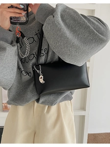 Detail of a black minimalist underarm bag featuring a metallic moon-shaped chain pendant