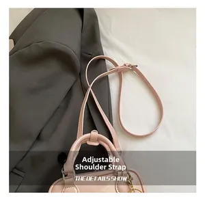 Detail of adjustable shoulder strap and leather handle on a pink crossbody square bag