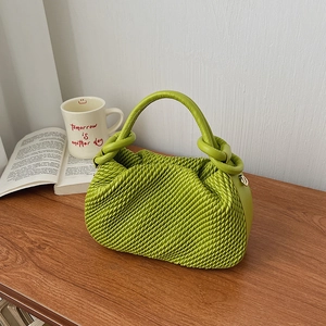 Detail of green pleated leather bucket bag with twisted handle on a wooden table