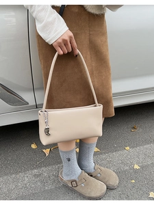 Beige rectangular underarm bag with metal chain detail shown in casual street style