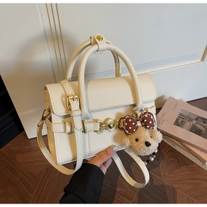Detail of cream leather handbag with gold heart clasp and plush dog pendant