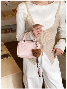 Pink patent leather crossbody bag with cute plush bear charm held by woman in vest