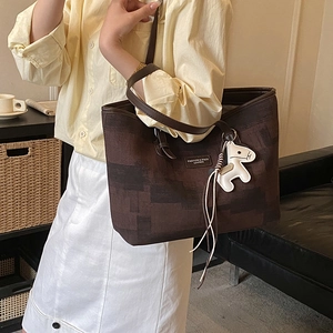 Detail of dark brown tote bag with artistic texture and leather horse charm accessory