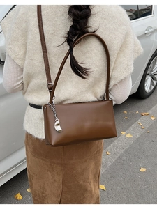 Detail of a dark brown glossy leather baguette bag with a silver chain charm on shoulder