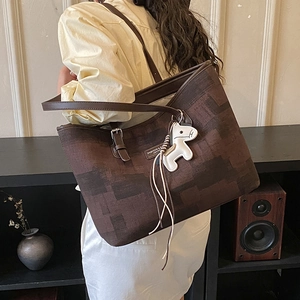 Detail of large tote bag with brown pattern and horse charm shown on shoulder