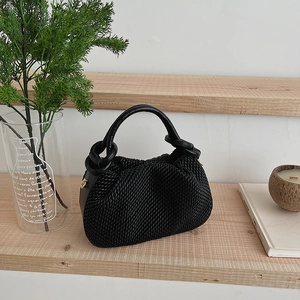 Detail of black woven texture bucket bag with gold hardware on a wooden shelf