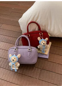Detail of burgundy and lavender suede boston bags with bear charms on wood floor