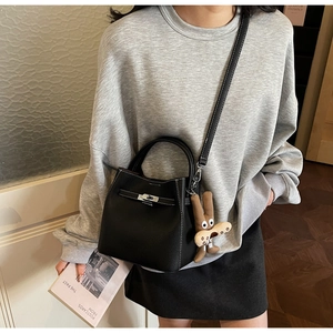 Detail of black leather bucket bag featuring a metal twist lock and cute plush pendant
