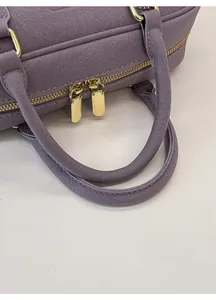 Detail view of purple handbag featuring grainy texture and comfortable padded handle
