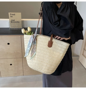 Detail of straw woven tote bag with brown leather handles and decorative floral silk scarf