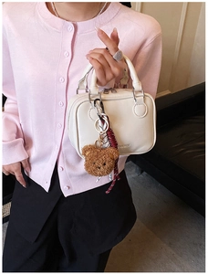 Close-up of a white leather mini bag with double handles and a cute plush bear accessory