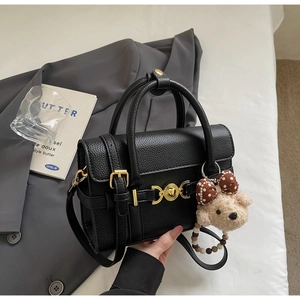 Detail of black lychee grain leather handbag with gold heart lock and bear charm