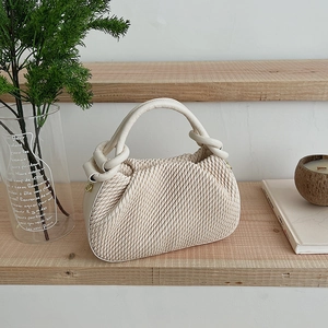 Detail of pleated beige bucket bag with knotted handle on a minimalist wooden shelf