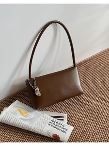 Detail of a brown leather shoulder bag with silver chain and moon pendant on woven mat