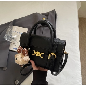Detail of black pebbled leather handbag with gold heart lock and plush dog charm accessory