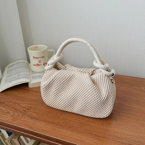 Close-up of the cream bucket bag with waffle texture and knotted handle detail