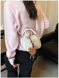 Close-up of creamy white leather handbag with double zipper and plush bear charm detail