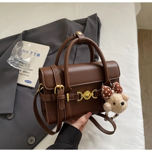 Detail of brown litchi pattern leather handbag with gold clasp and teddy bear charm