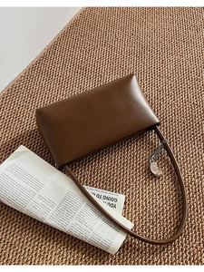 Detail of dark brown leather underarm bag with silver metallic charm on woven texture