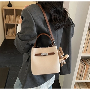 Detail of cream bucket bag with litchi texture, brown straps, and silver turn-lock closure