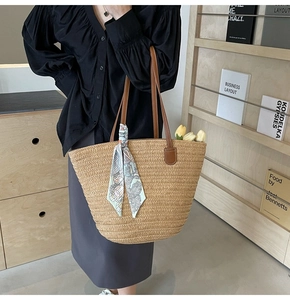 Detail of straw tote bag with brown leather straps and a decorative green silk scarf