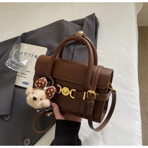 Detail of dark brown lychee texture handbag with gold buckle and plush bear charm