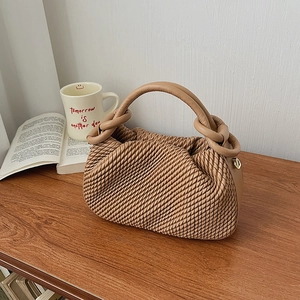 Detailed view of beige bucket bag with pleated texture and golden metal ring accents