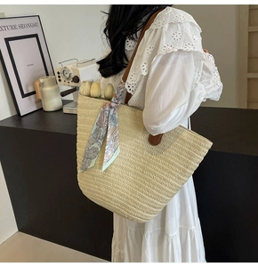 Detail of a large straw tote bag with brown leather straps and floral silk scarf accessory