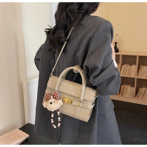 Close-up of beige lychee leather handbag with a cute plush bear charm on a grey blazer