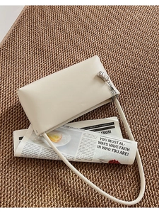 Detail of minimalist cream leather shoulder bag with silver buckle on newspaper