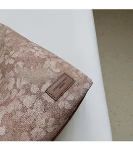 Detail shot of beige floral jacquard fabric and brown leather logo patch on the tote bag