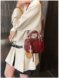 Detail of burgundy glossy crossbody bag featuring dual zippers and cute bear charm