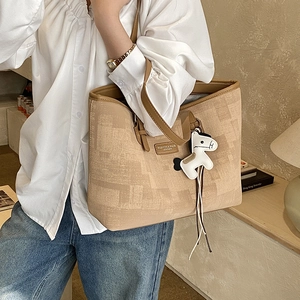 Detail of canvas tote bag with woven texture, leather trim and a horse pendant charm