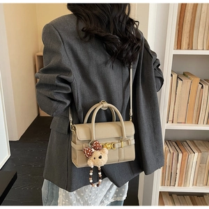 Detail view of a beige pebble leather handbag with a plush bear charm on a bookshelf