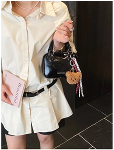 Detail of black patent leather crossbody bag with teddy bear charm and striped ribbons