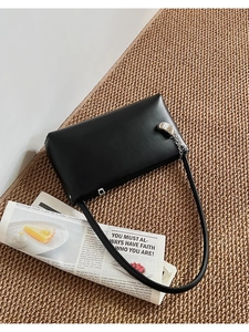 Detail of black leather shoulder bag with silver metal chain on a woven mat