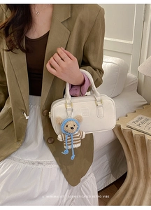 Detail of white Boston handbag with textured leather, gold hardware and brown bear charm